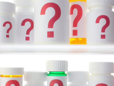 Close crop of medicine cabinet filled with pill bottles, each labeled with a red question mark.